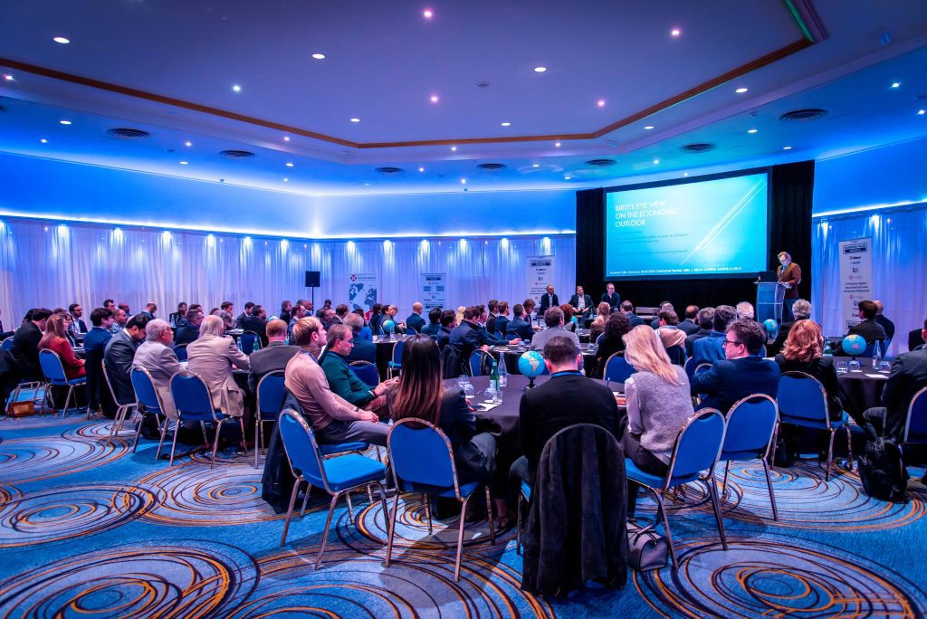 International Business Networking Event - Audience attending a business conference with a speaker presenting on stage in a blue-lit room